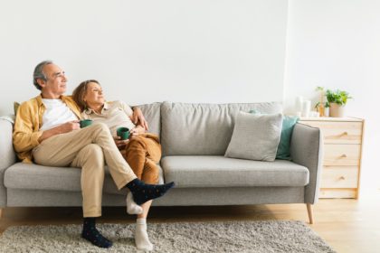 Happy long-lasting marriage. Senior husband and wife hugging, drinking coffee resting on sofa