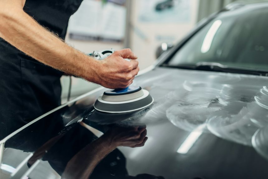 Male person with polishing machine cleans car hood