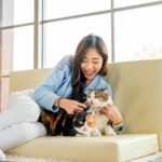 Side view pretty Asian woman give cat food in plastic package to her cat and stay with other cat