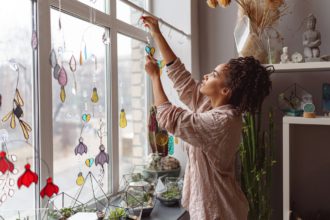 Woman holding handmade glass decoration in the form of heart standing in home decor studio